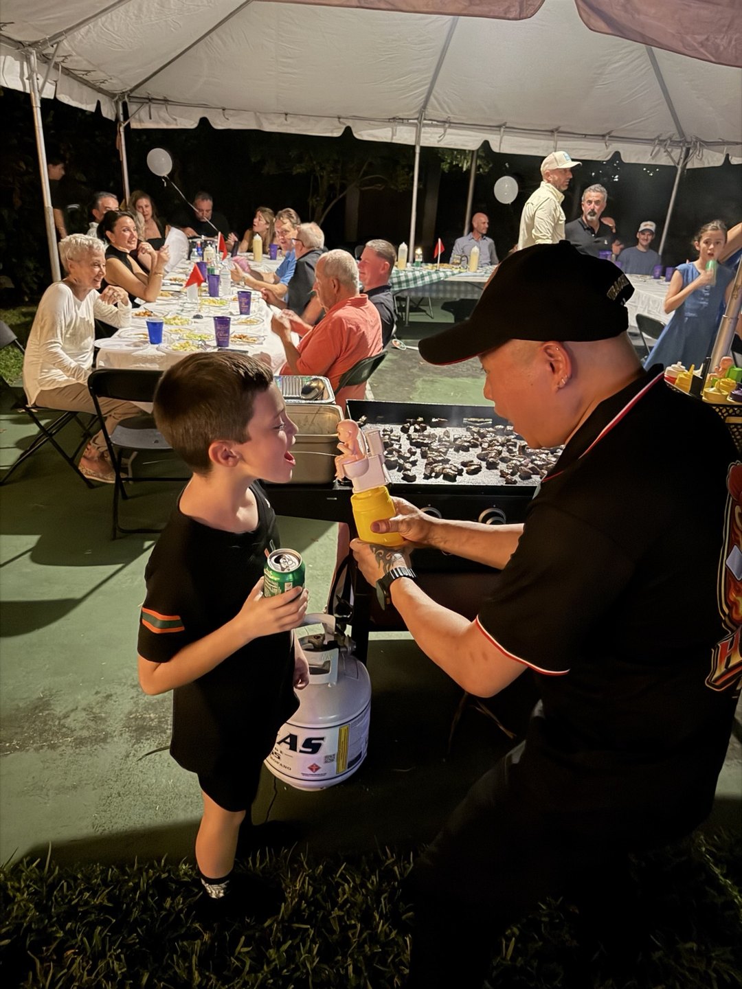 Hibachi C2 chef entertaining a young guest beside the grill at a family celebration